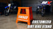 Orange dirt bike stand with '562 Arredondo' branding in a garage setting with motorcycles.